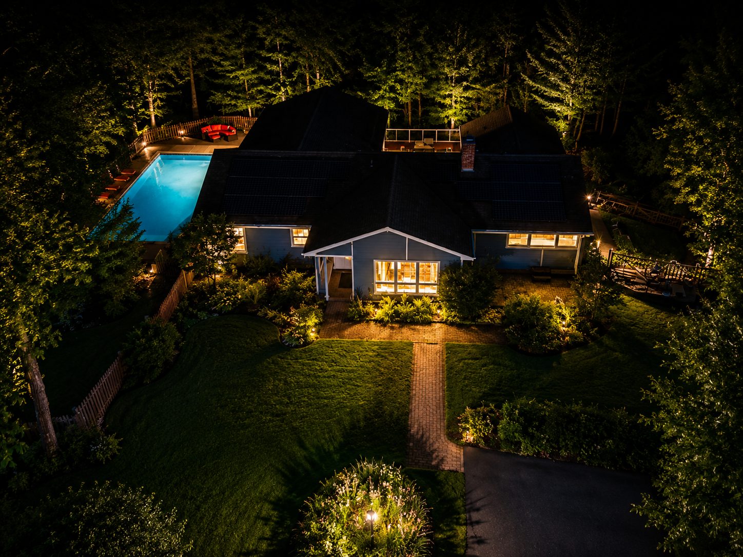 Gamblewood at twilight — glowing home and lit pool from above